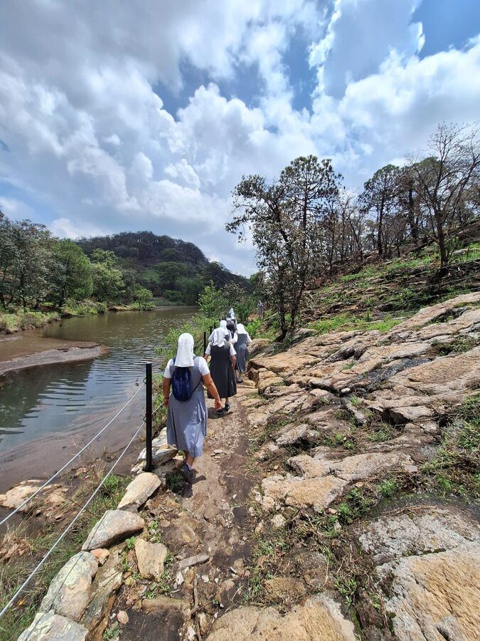 Un grupo de hermanas camina en fila por un sendero de piedra junto a un lago.