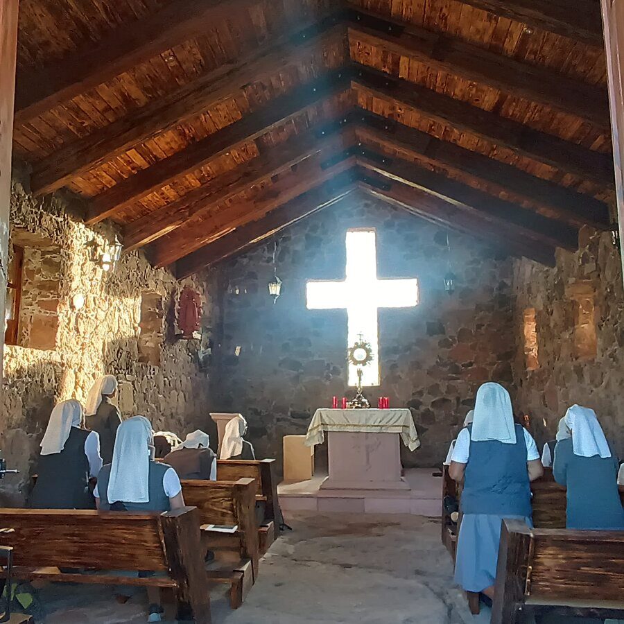 Varias hermanas rezan en la capilla frente al Santísimo, bajo una ventana en forma de cruz.