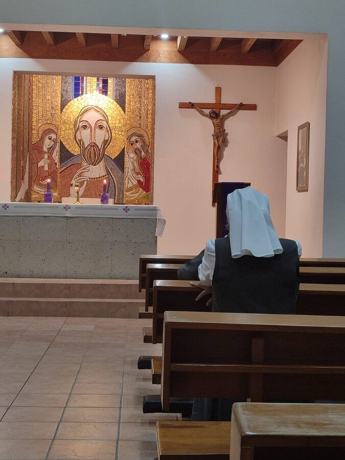 Una hermana reza sola en la capilla, frente al mosaico de Cristo y el crucifijo.
