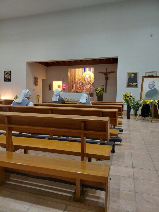 Hermanas en oración en los bancos de la capilla, ante el mosaico de Cristo y unos girasoles junto al altar.